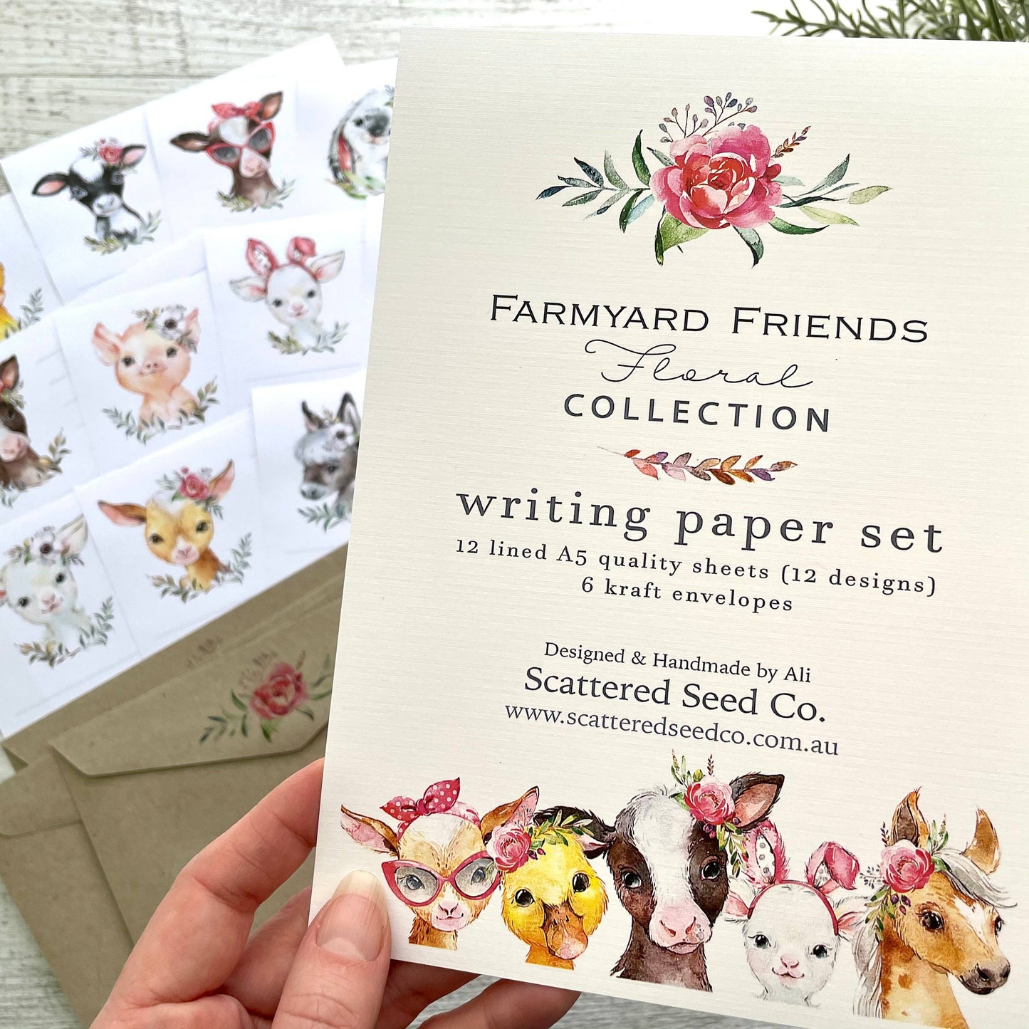 Writing paper set with farmyard animal illustrations and floral designs, held by a hand.