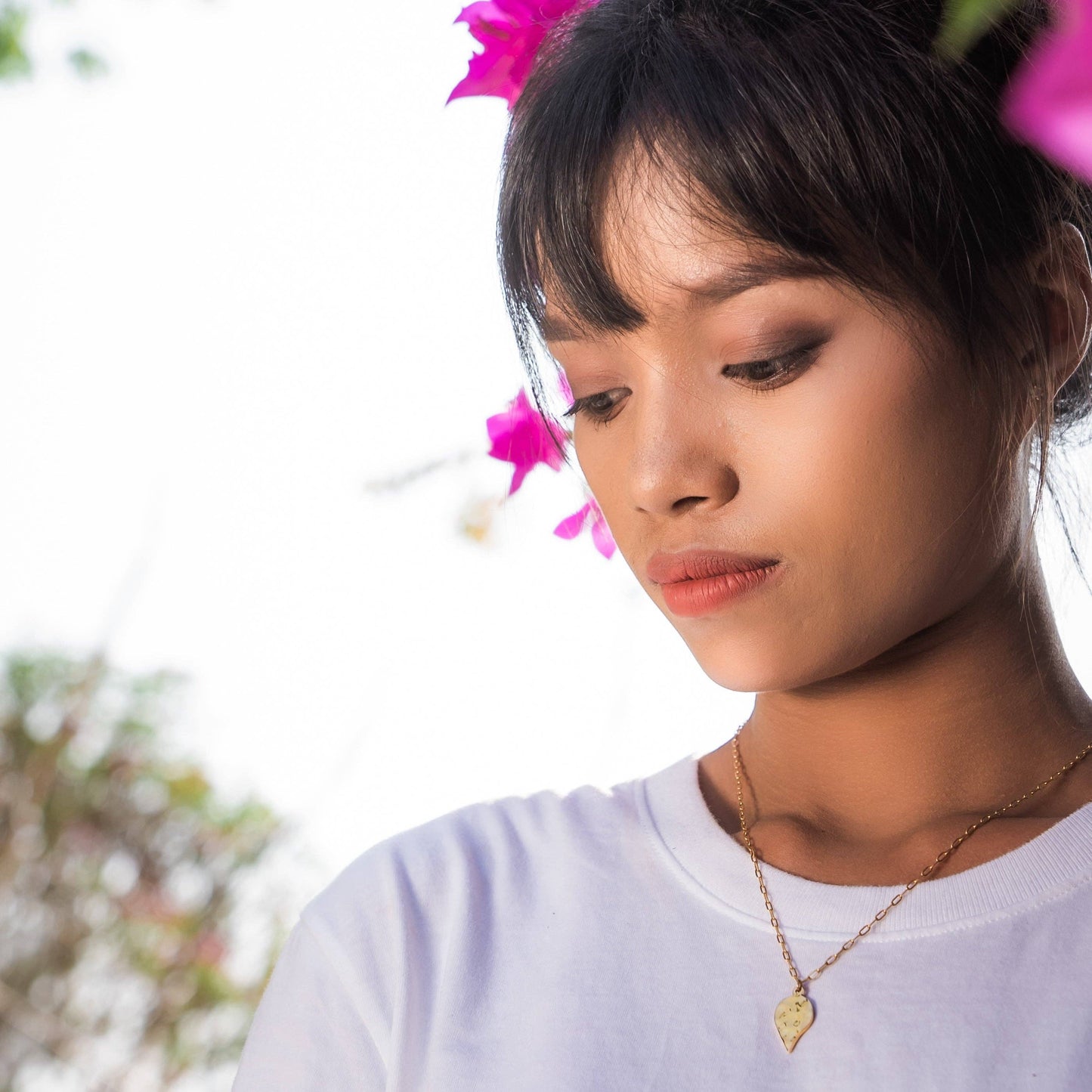 Woman with flowers in her hair wearing a white shirt and gold necklace.