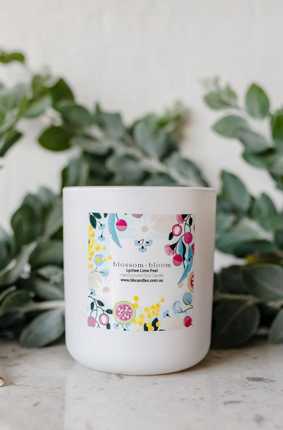 A white candle labeled "blossom + bloom" with packaging featuring colorful floral patterns. Then scent is "Lychee Lime Peel."