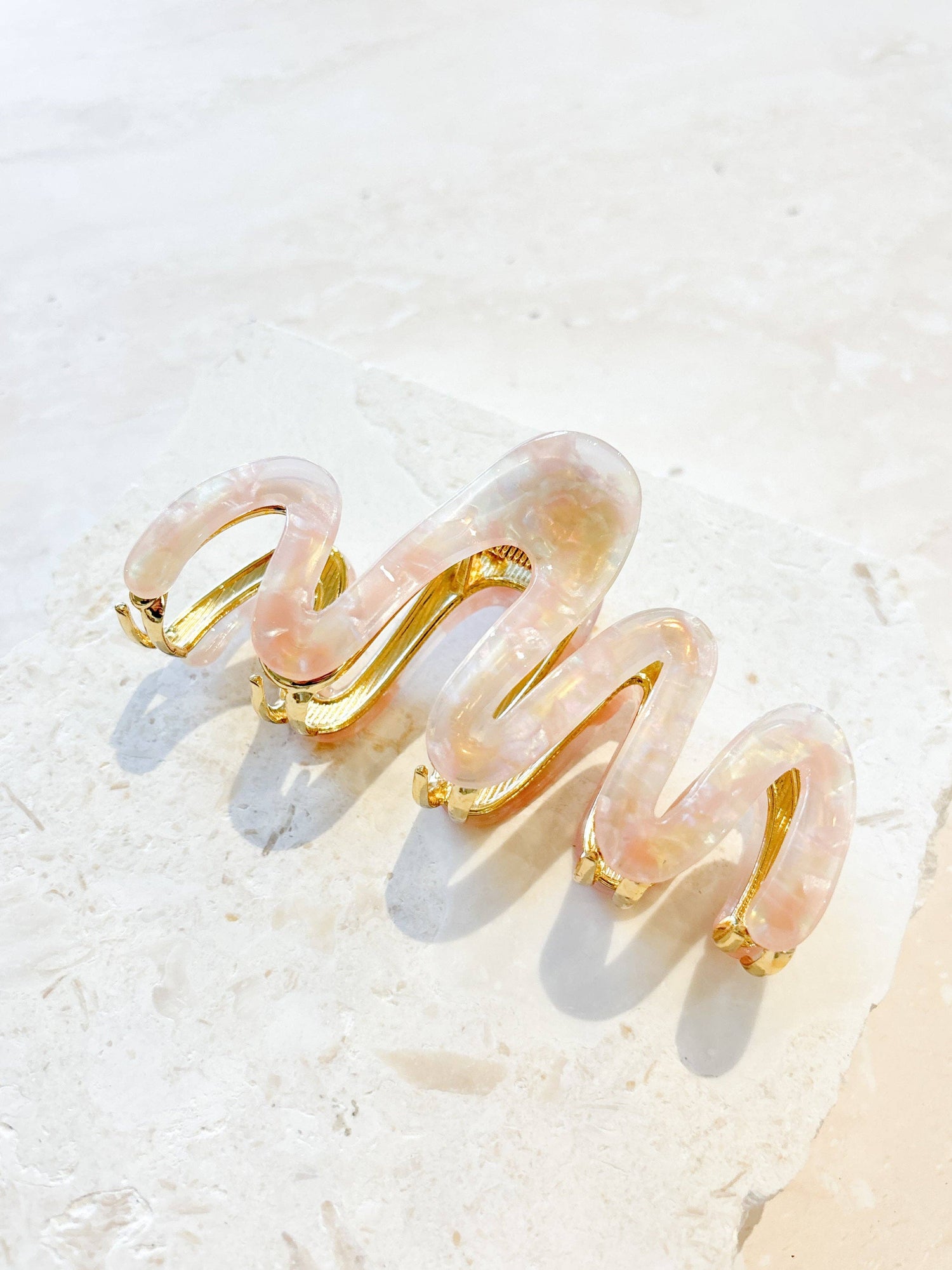 A range of Wave Acrylic Metal Claw Clips by Angels Whisper Accessories, displayed in various colours. The clips feature a stylish wavy design with a sturdy metal clasp.