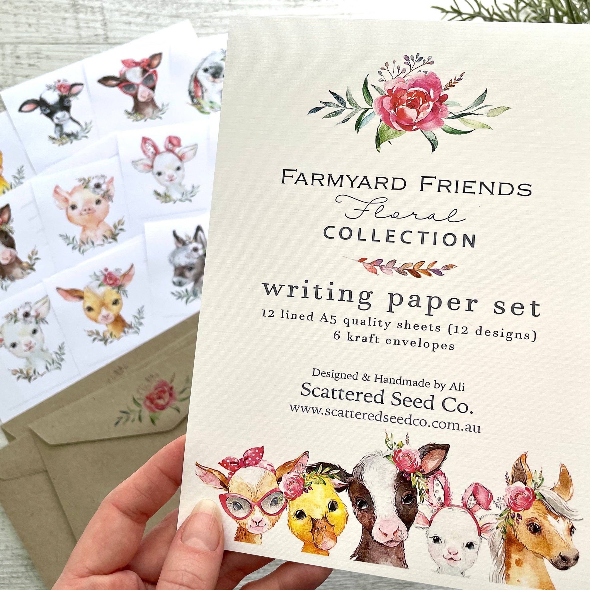 Writing paper set with farmyard animal illustrations and floral designs, held by a hand.