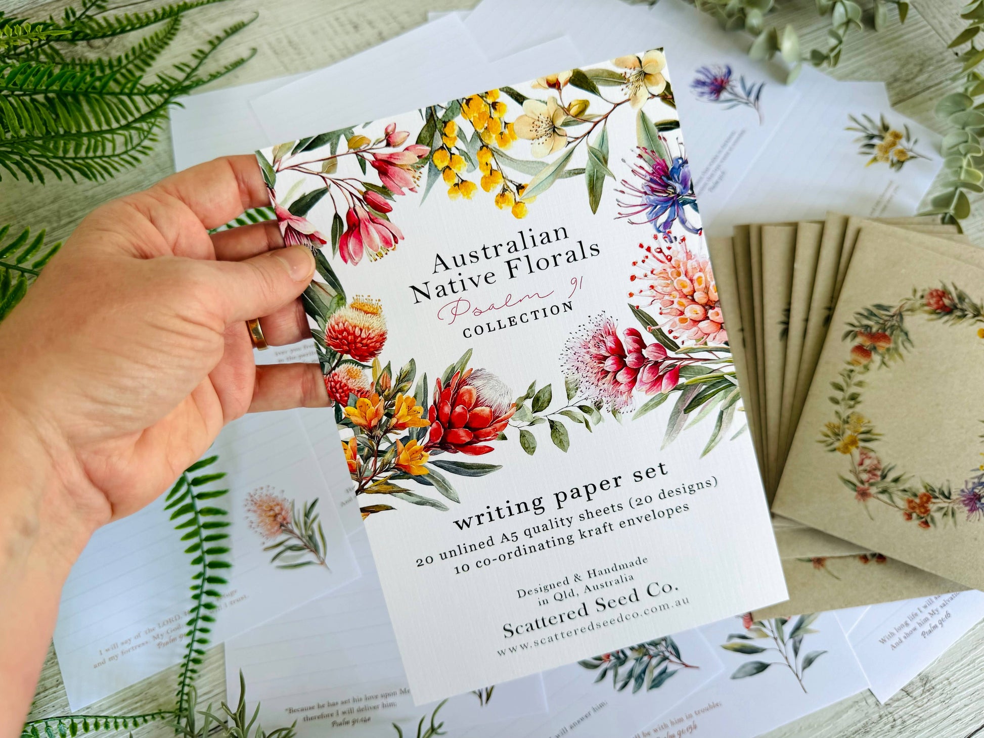 Hand holding a writing paper set with Australian native floral designs on a table with more sets.