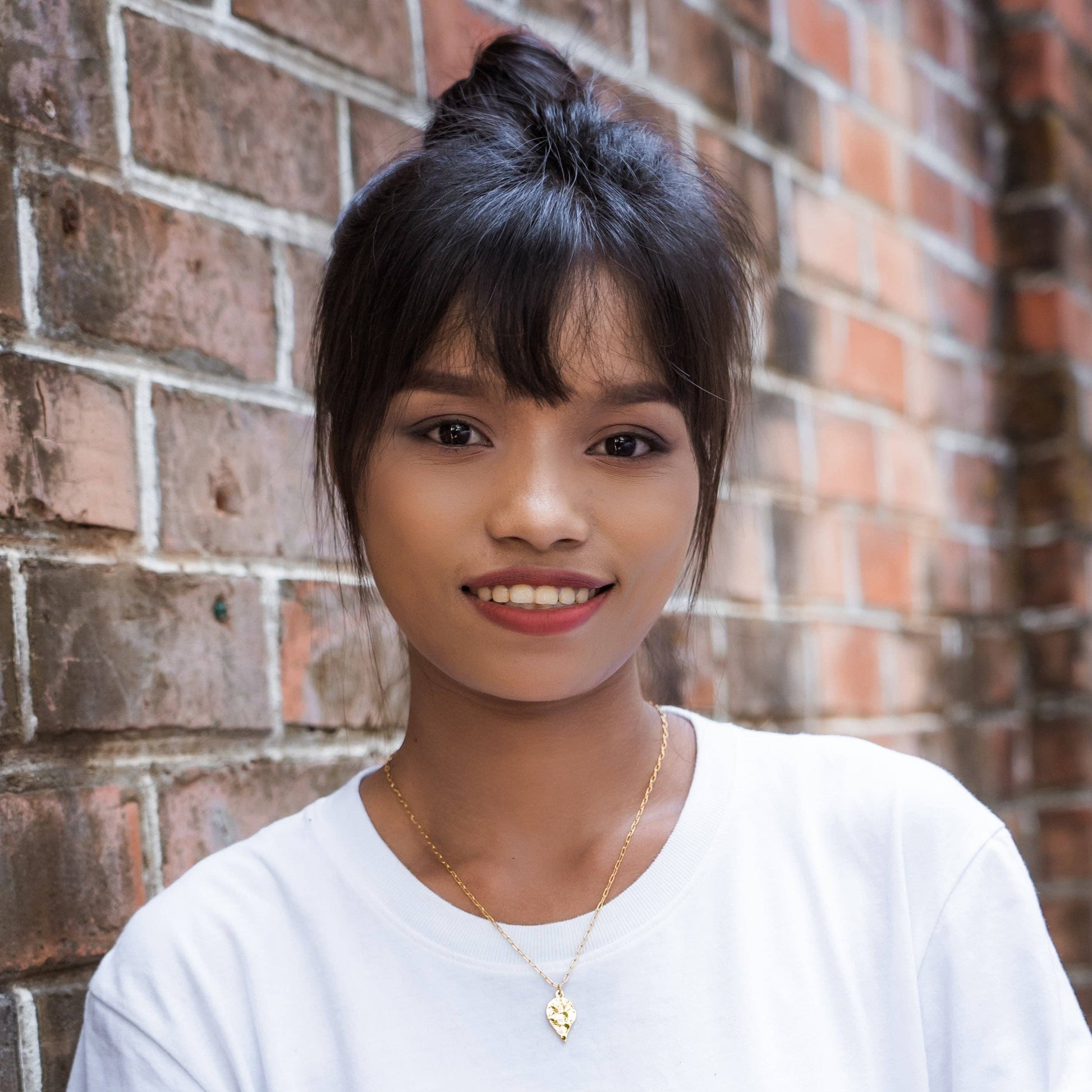 Woman wearing a white shirt and gold necklace against a brick wall