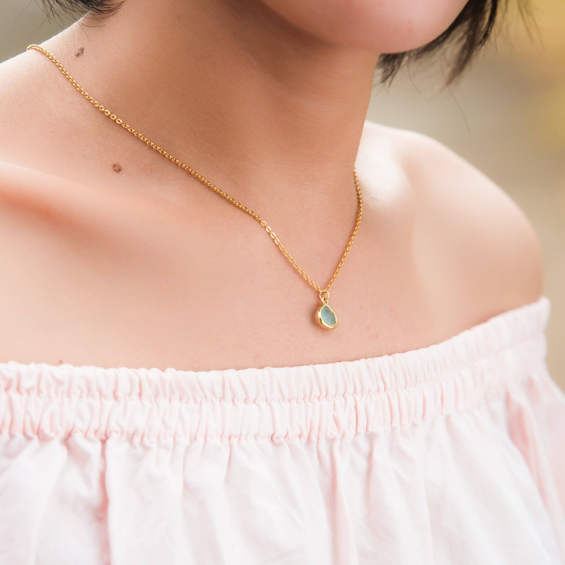 Desert Sunrise gold necklace with a green pendant worn by a person in a light pink top.