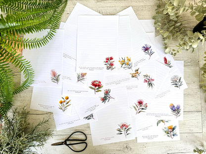 Sheets of paper with scriptures written on them and floral illustrations on a wooden surface with greenery.