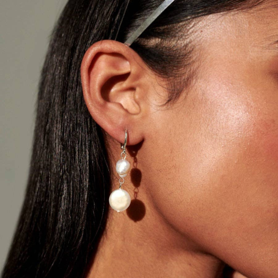 A close-up image of a person wearing silver-plated double pearl drop earrings.