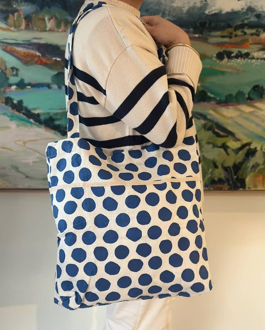 Lady holding a cream linen tote bag with navy polka dots over her shoulder. It features sturdy handles and a relaxed roomy shape—perfect for everyday use.