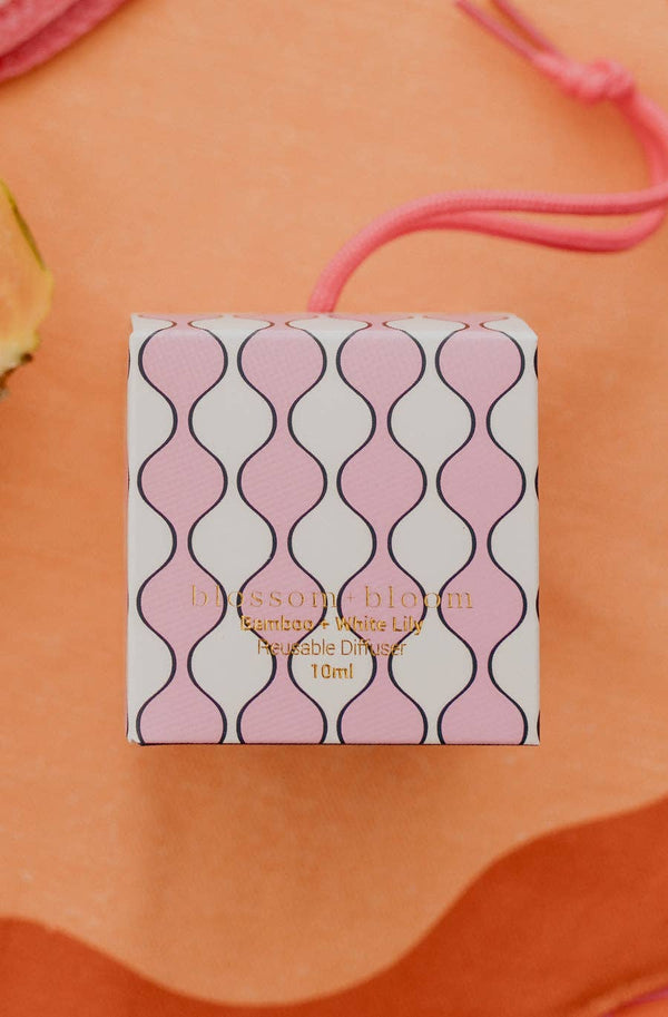 A small diffuser box labeled " blossom + bloom" with a pink wavy pattern on it and the scent is "Bamboo + White Lily."