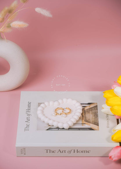 Styled arrangement on a pink background featuring a heart shaped bubble trinket tray holding a pair of gold earrings.