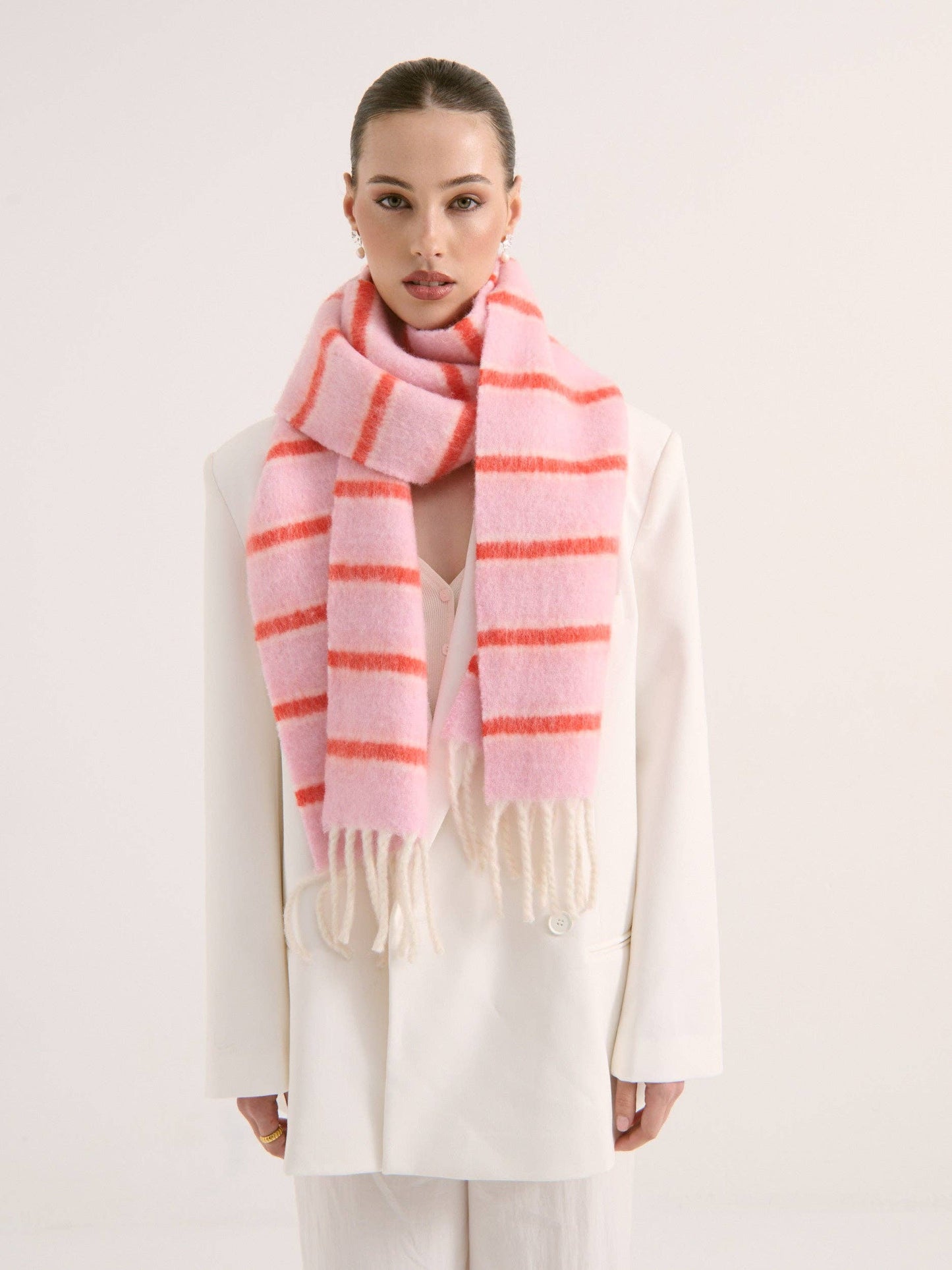 Lady wearing a pink and orange fluffy striped scarf on a white background
