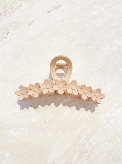Nude daisy claw clip with a row of delicate flower shapes. The claw clip is set against a light textured background casting a subtle shadow.