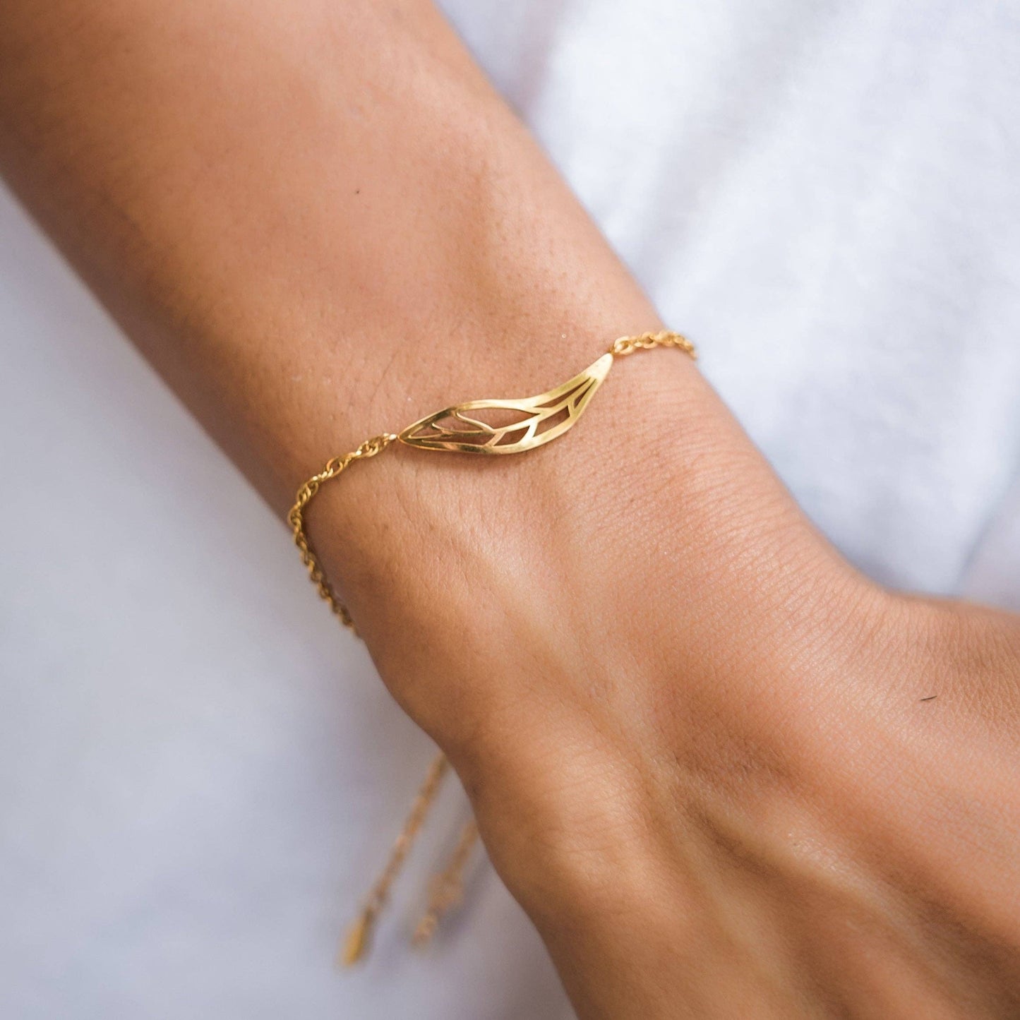 Gold bracelet with leaf design on a wrist against a white background