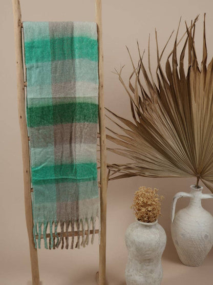 Fluffy oversized scarf in green and beige tones draped over a wooden ladder.