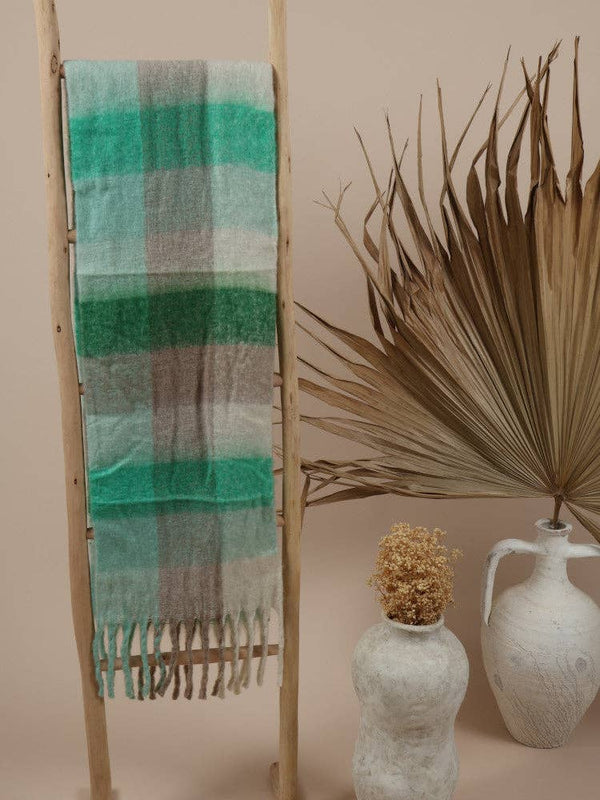 Fluffy oversized scarf in green and beige tones draped over a wooden ladder.