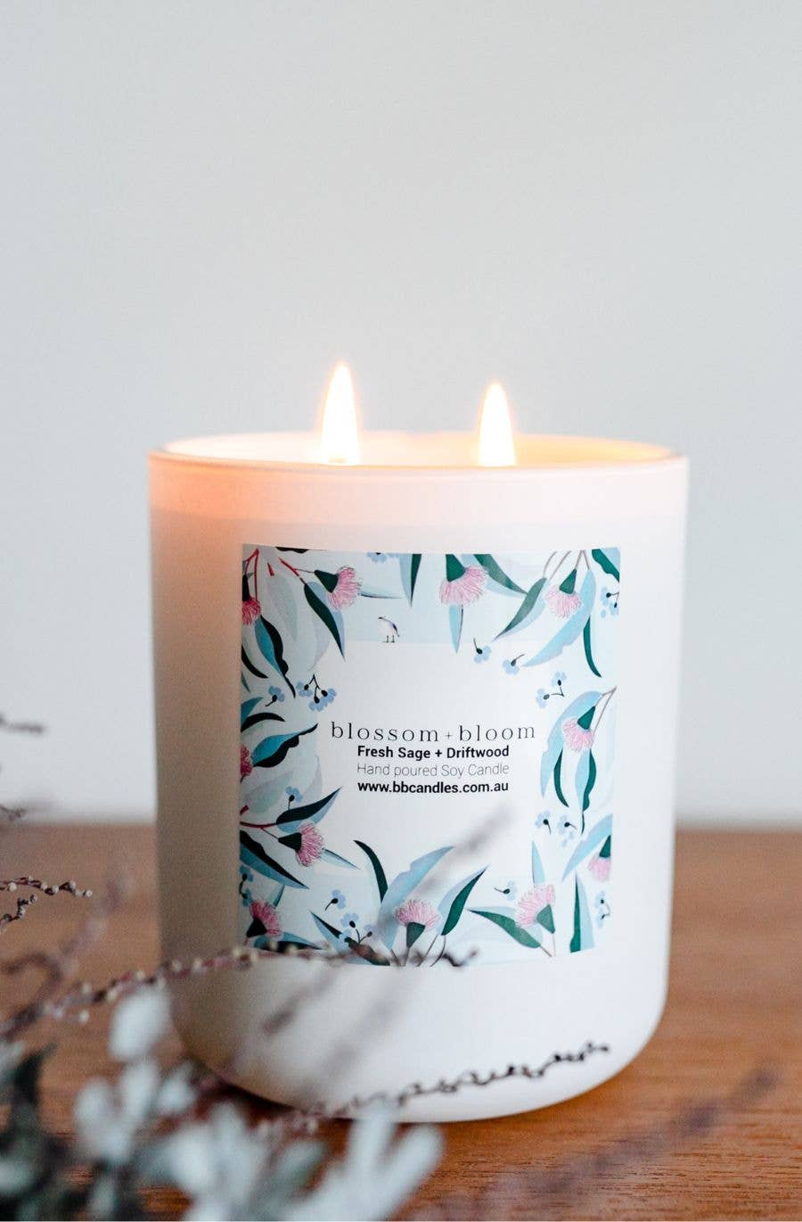 A white candle labeled "blossom + bloom" with colorful floral patterns. The scent is "Fresh Sage + Driftwood."