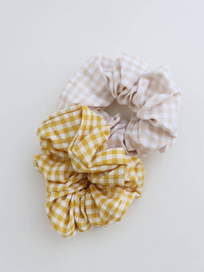 Two scrunchies, one yellow checkered and one beige gingham, on a white background