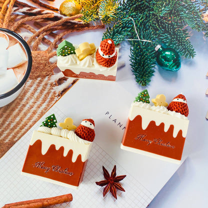 Three Handmade Artisan Christmas Soaps | Christmas Fantasia | Champagne & Strawberry Scent— arranged on a tabletop with pine branches, ornaments, a cinnamon stick, star anise, and a bowl of marshmallows. The pieces are brown with cream-colored frosting details and topped with miniature trees, stars, and Santa figures.