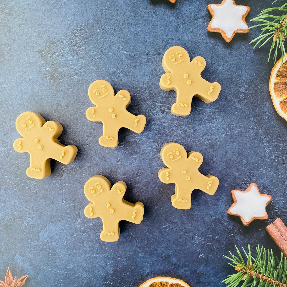 Five Handmade Artisan Christmas Soap | Gingerbread Man | Warm Gingerbread, Caramel & Vanilla arranged on a dark textured surface with holiday props including star-shaped cookies, pine needles, cinnamon, and dried orange slices.