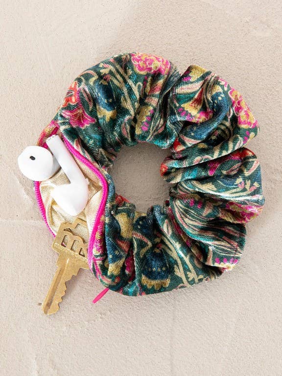 Multicolored/green velvet scrunchie with earphones and keys in zipper pocket-on a beige surface.