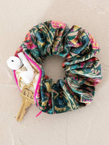 Multicolored/green velvet scrunchie with earphones and keys in zipper pocket-on a beige surface.
