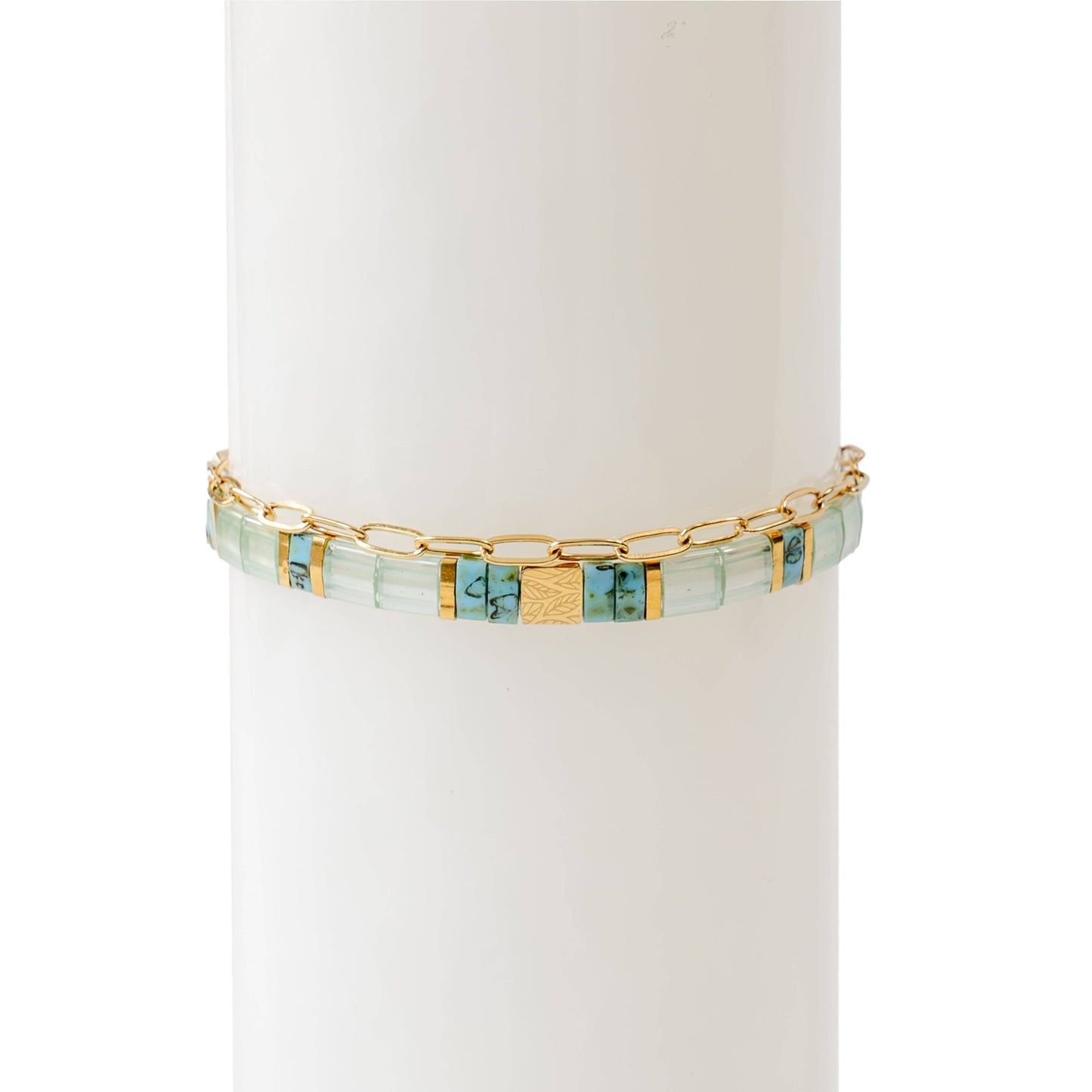 A two-piece bracelet stack displayed on a white cylindrical stand. The first bracelet features hand-strung rectangular glass beads in soft turquoise, blue, and gold tones, with central 18K gold-plated stainless steel bead engraved with a delicate leaf motif. The second bracelet is a thin, 18K gold-plated stainless steel oval chain, adding an elegant and minimal touch The combination of colours and textures creates a refined yet artistic look.