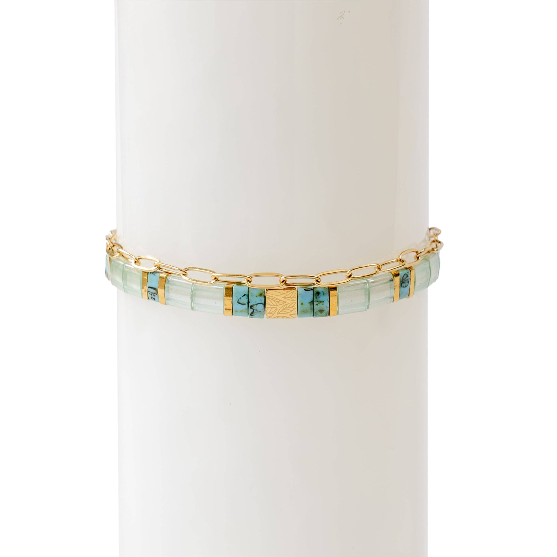 A two-piece bracelet stack displayed on a white cylindrical stand. The first bracelet features hand-strung rectangular glass beads in soft turquoise, blue, and gold tones, with central 18K gold-plated stainless steel bead engraved with a delicate leaf motif. The second bracelet is a thin, 18K gold-plated stainless steel oval chain, adding an elegant and minimal touch The combination of colours and textures creates a refined yet artistic look.