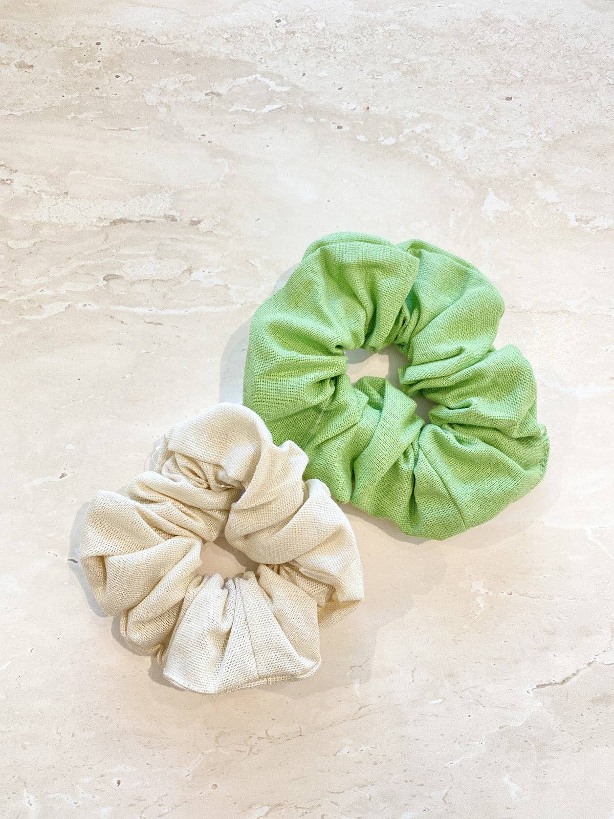 Two scrunchies, one green and one beige, on a light beige surface.