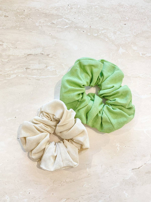Two scrunchies, one green and one beige, on a light beige surface.