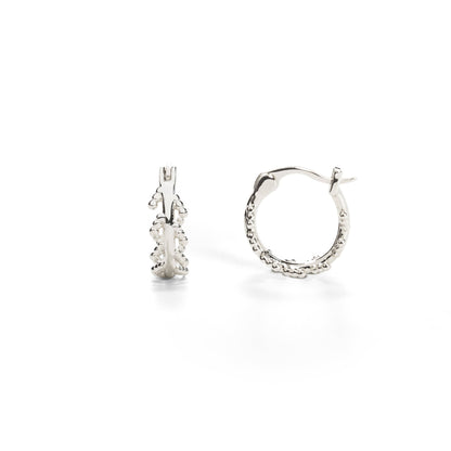 A pair of white gold-plated hoop earrings with an intricate leaf design inspired by the mustard plant.