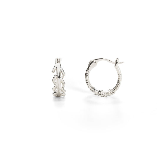 A pair of white gold-plated hoop earrings with an intricate leaf design inspired by the mustard plant.