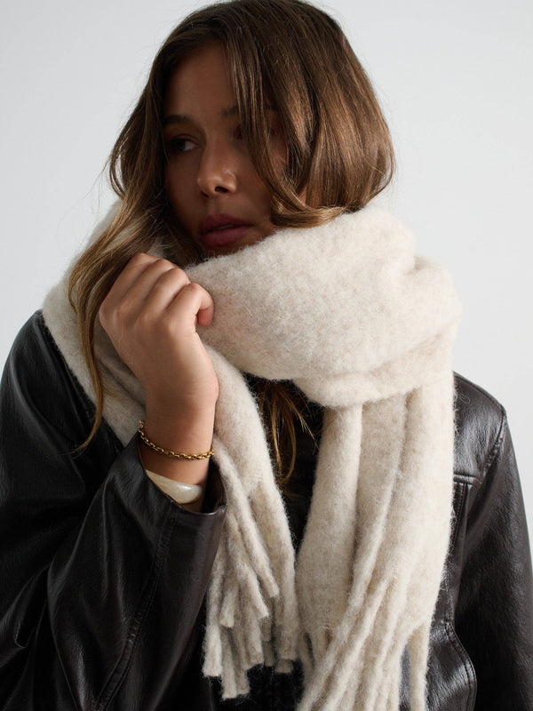Person wearing a oatmeal scarf with a plain background