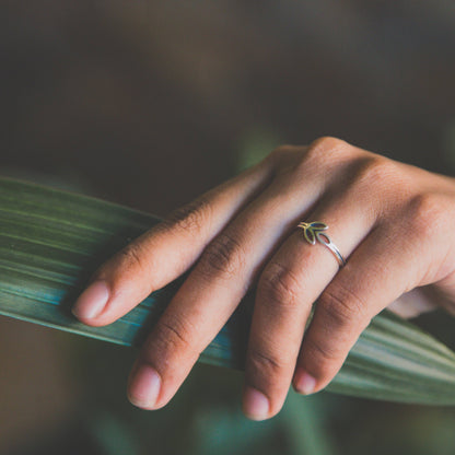 A delicate sterling silver ring featuring a olive branch design worn on a person's finger while resting on a green leaf.