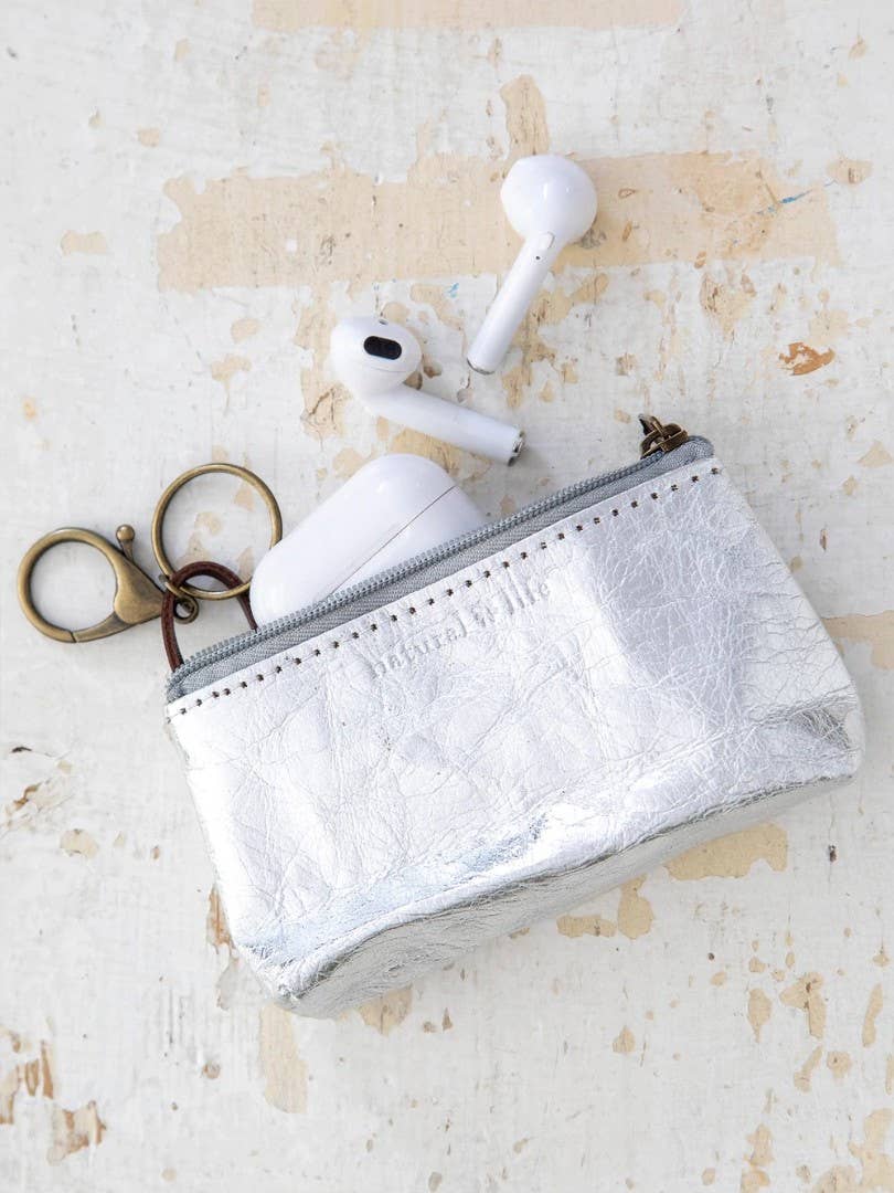 Small silver pouch with a keychain and wireless earbuds on a textured beige surface