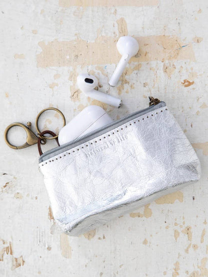 Small silver pouch with a keychain and wireless earbuds on a textured beige surface