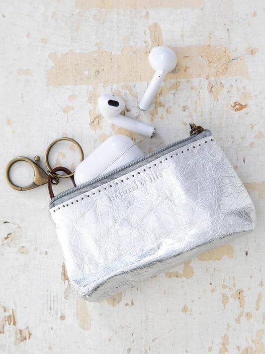 Small silver pouch with a keychain and wireless earbuds on a textured beige surface
