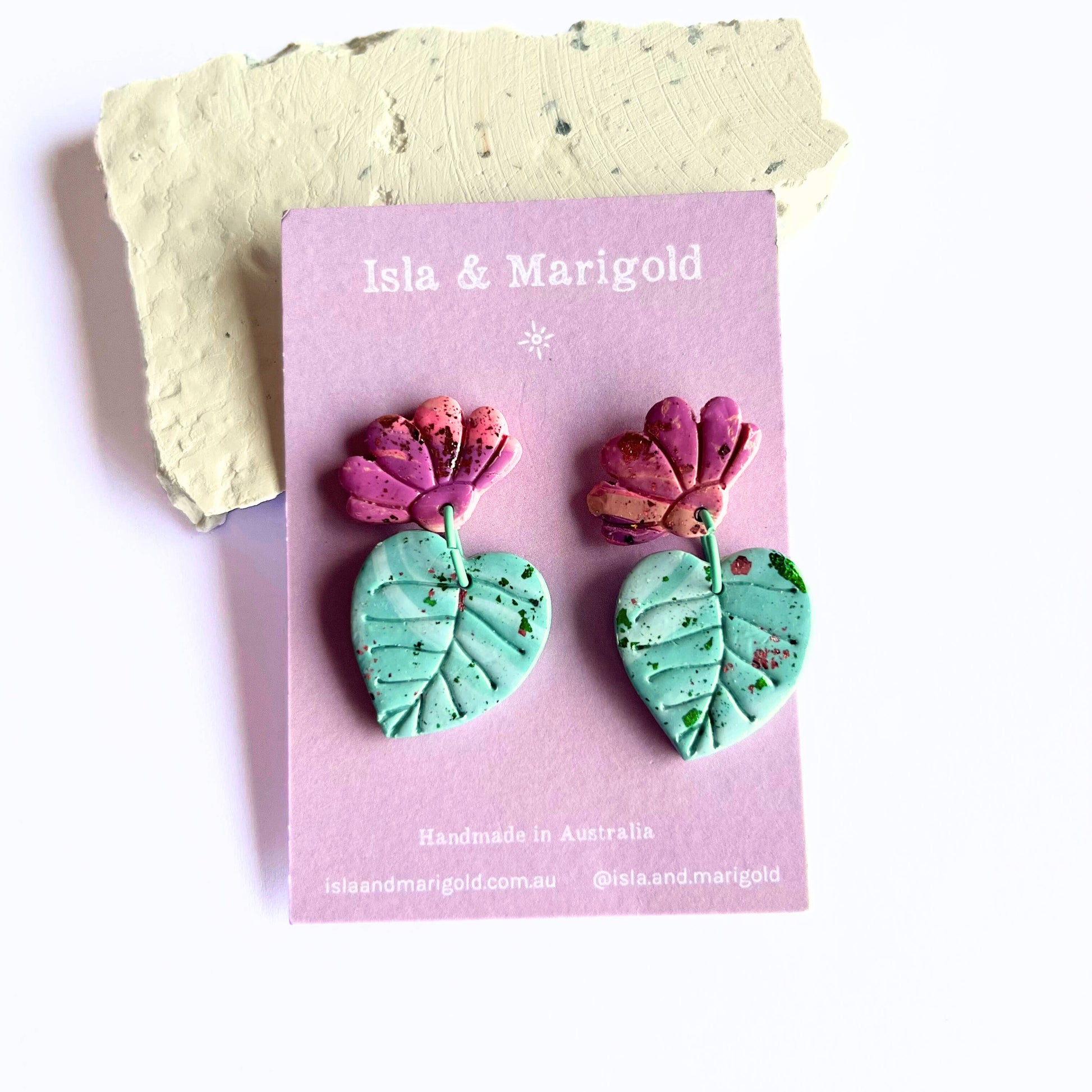 Handmade polymer clay earrings with pink flowers and green leaf drops on Isla & Marigold display card.