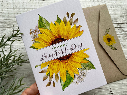 Greeting card with sunflowers and 'Happy Mother's Day' text, accompanied by a matching envelope on a wooden surface.