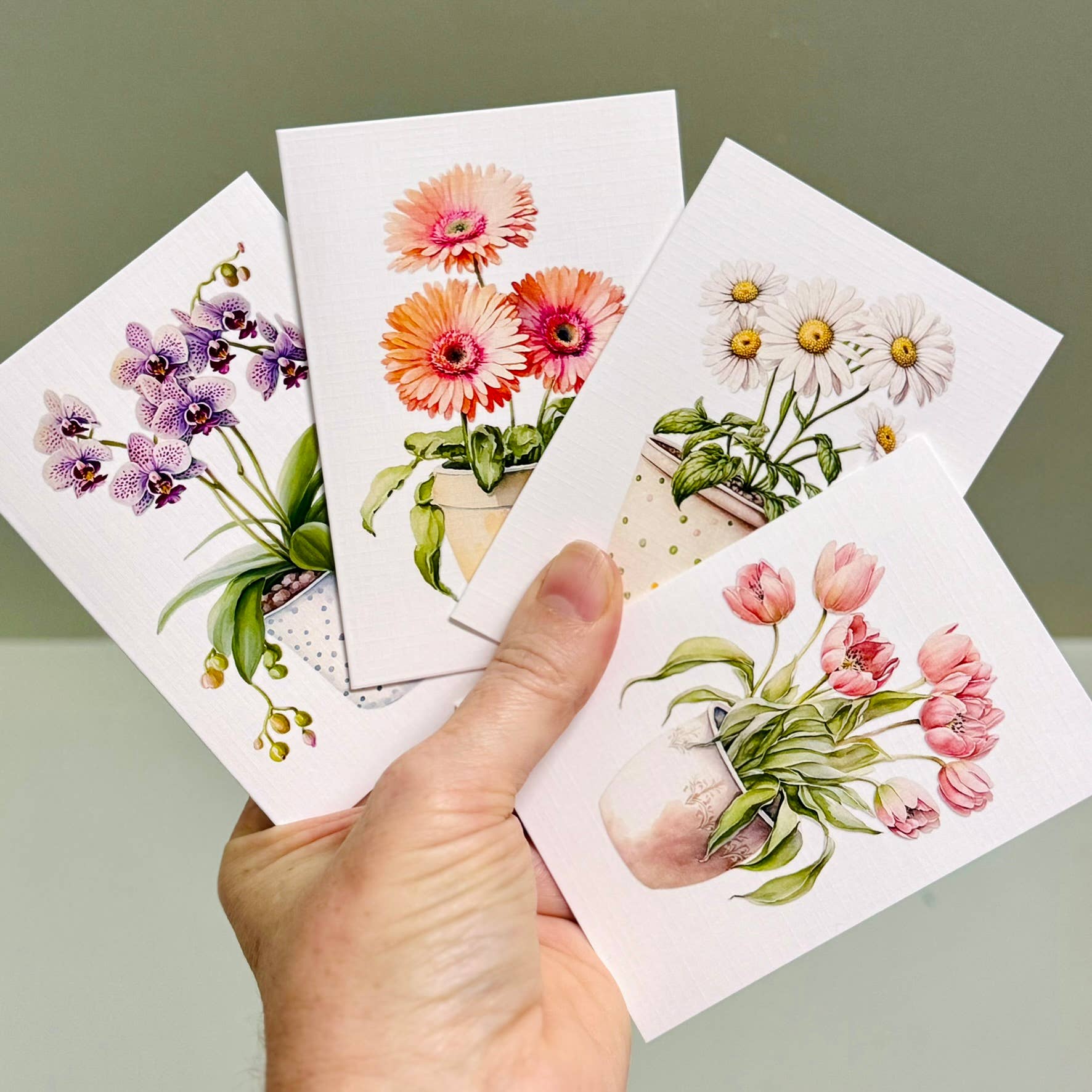 Set of floral mini greeting cards held by a hand against a plain background