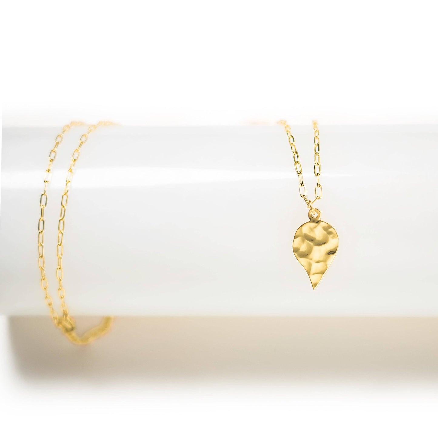 Gold necklace with a leaf-shaped pendant on a white background
