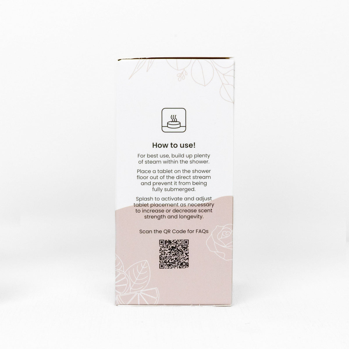 The back of a white product box of Shower Steamer Treat Pack with a light pink lower section, featuring a 'How to use!' icon, instructions, a QR code, and faint floral line art on a white background.
